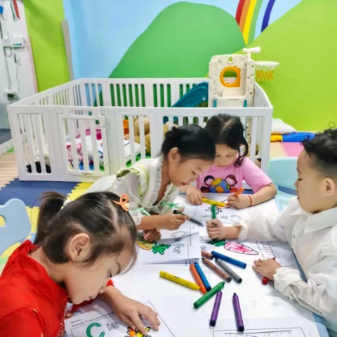 Preschoolers colouring 'C is for carrot' worksheets with chunky crayons at a shared table