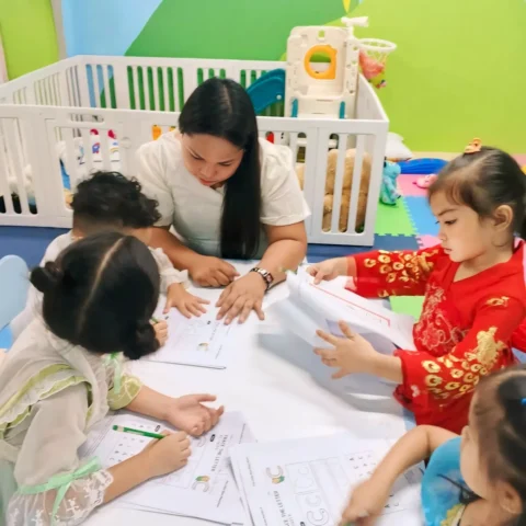 Teacher guiding a small group of preschoolers as they trace the letter C on worksheets at a low table