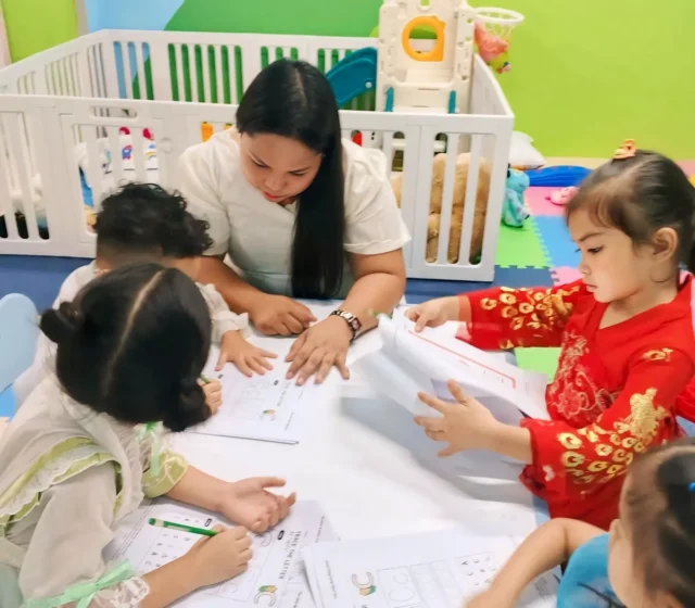 Teacher guiding a small group of preschoolers as they trace the letter C on worksheets at a low table