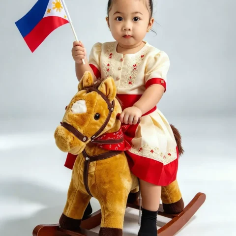 Toddler in a Filipiniana dress waving a Philippine flag while riding a plush rocking horse